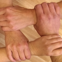 Vier Hände, die durch Greifen der Handgelenke ein Viereck formen.